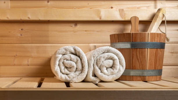 Two rolled towels and a wooden bucket on a wooden bench in a sauna.